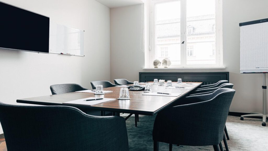 Moderner Boardroom mit großem Konferenztisch, eleganten Stühlen, Präsentationstechnik und natürlichem Tageslicht im Hotel The Wellem Düsseldorf.
