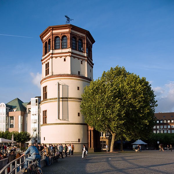Schlossturm am Burgplatz in der Düsseldorfer Altstadt bei sonnigem Wetter mit Besuchern am Rheinufer nahe dem Hotel The Wellem