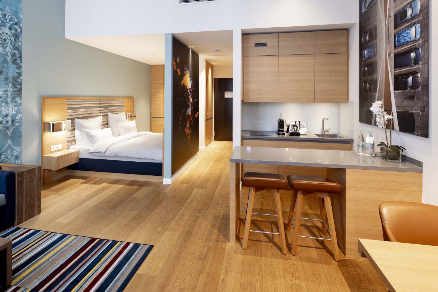 Business Suite im Hotel The Wellem Düsseldorf mit modernem Wohn- und Schlafbereich, offenem Küchenblock, hochwertigem Holzinterieur und elegantem Design.