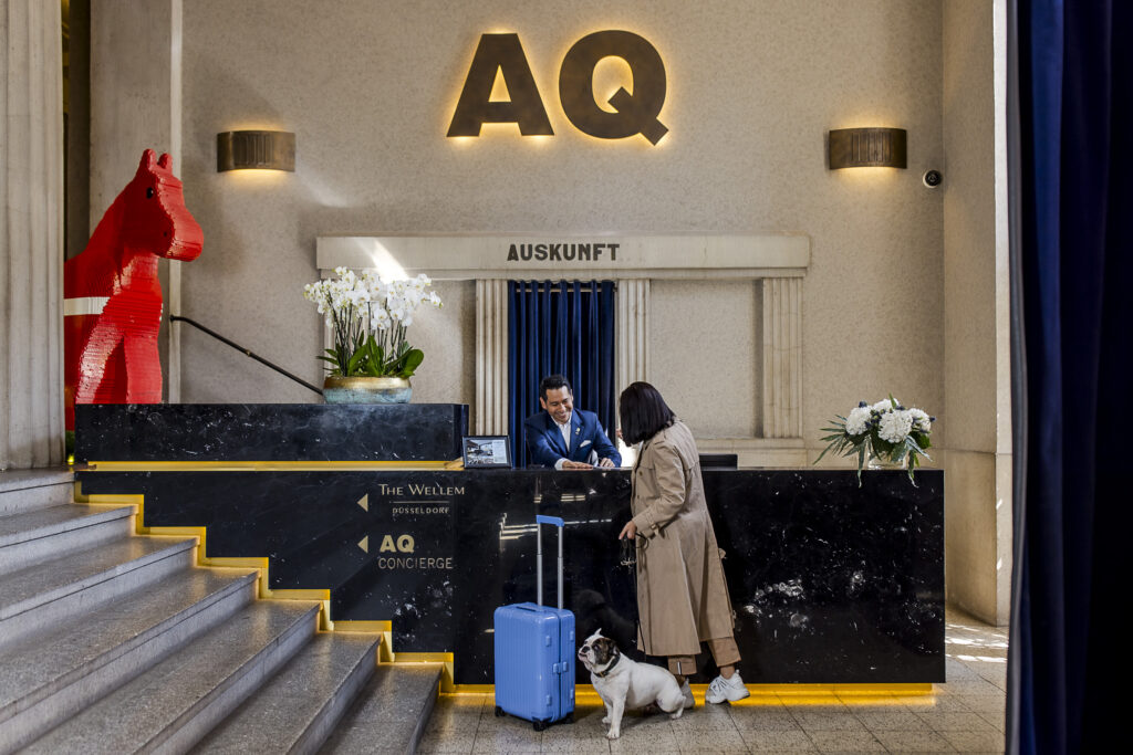 Concierge Service im Hotel The Wellem in Düsseldorf mit Gast an der Rezeption und Hund, im Eingangsbereich.
