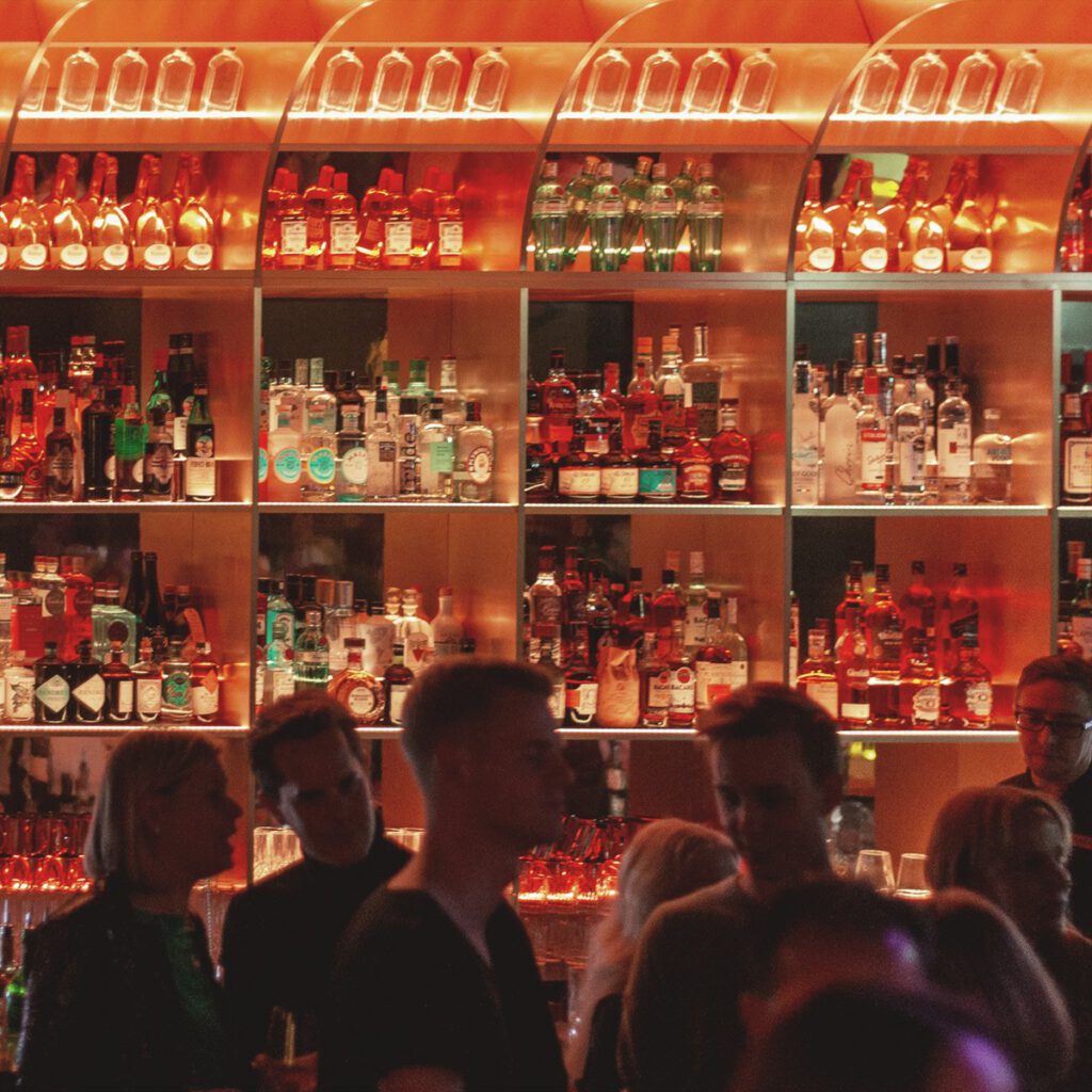 Stylische Baratmosphäre mit beleuchteter Flaschenwand und Gästen im Franks Club im Andreas Quartier Düsseldorf, Teil des exklusiven Nightlife-Erlebnisses des Hotel The Wellem.