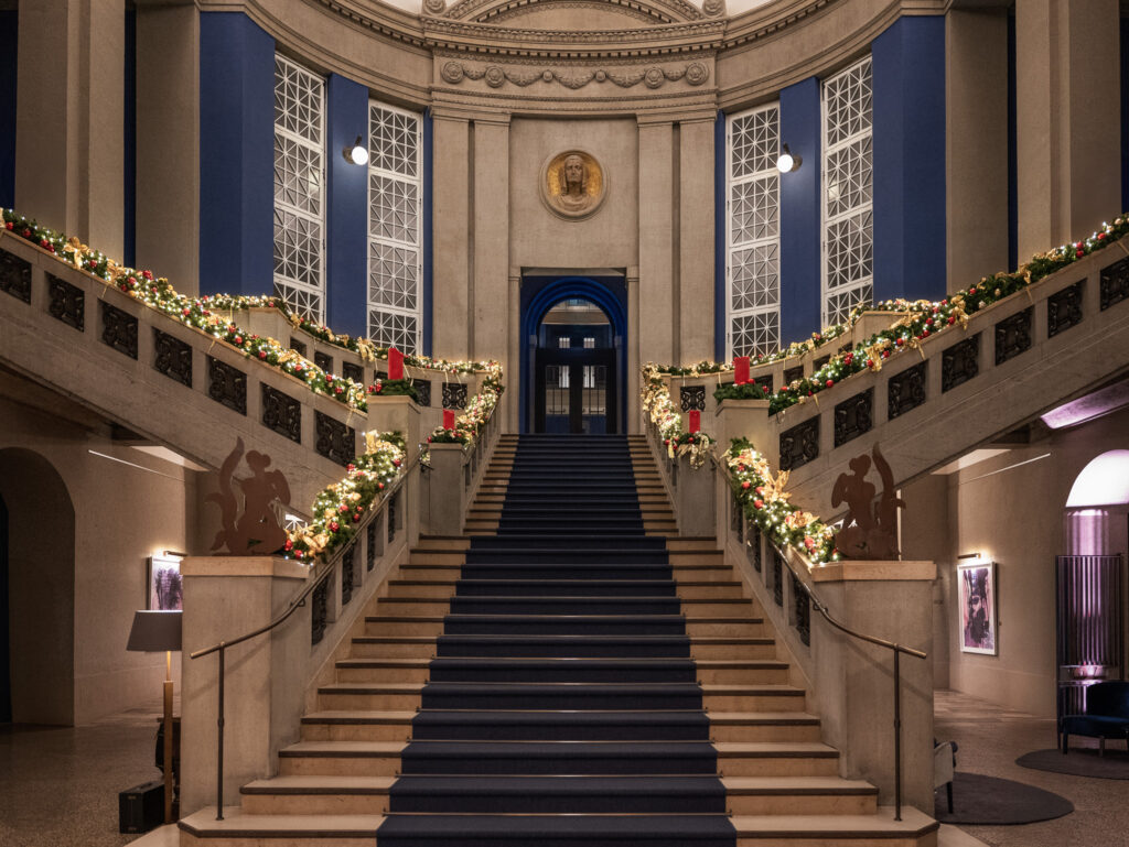 Festlich geschmückte historische Freitreppe im Hotel The Wellem Düsseldorf mit opulenter Weihnachtsbeleuchtung, Kränzen, roten Kerzen und elegant beleuchteter klassizistischer Architektur.